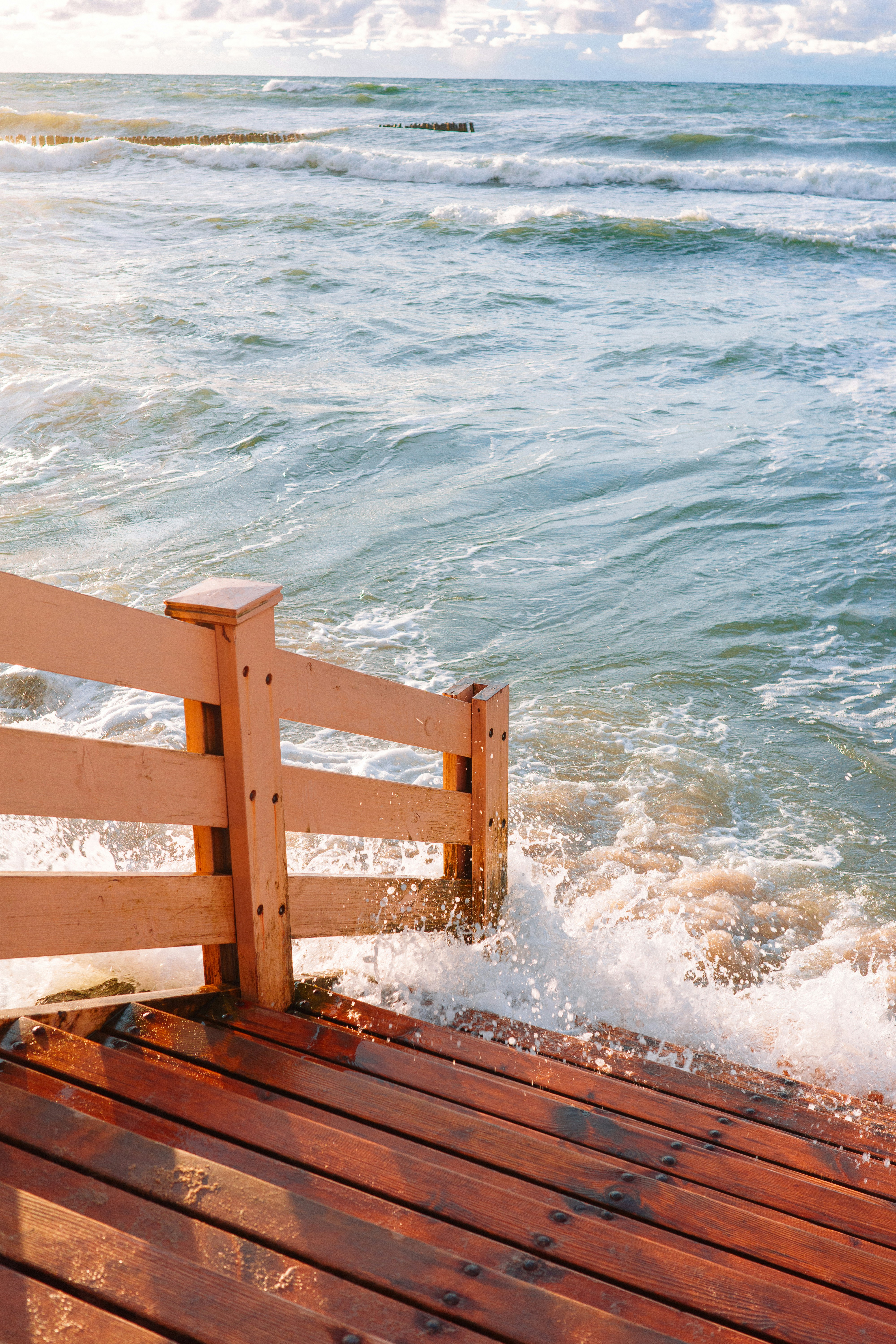 beach pier leading to ocean with waves splashing on it